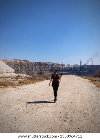 A woman is walking through mining to take pictures. View of open cast mining quarry with machinery at work. This area has been mined for copper, silver, gold, and other minerals, based in Serbia 