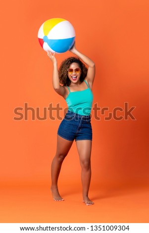Pretty smiling African American woman in casual summer clothes with colorful beach ball on orange background