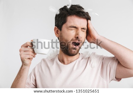 Image of caucasian man 30s with bristle in casual t-shirt drinking coffee while standing under falling feathers isolated over white background