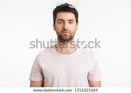 Image of morning man 30s with bristle in casual t-shirt standing under falling feathers isolated over white background