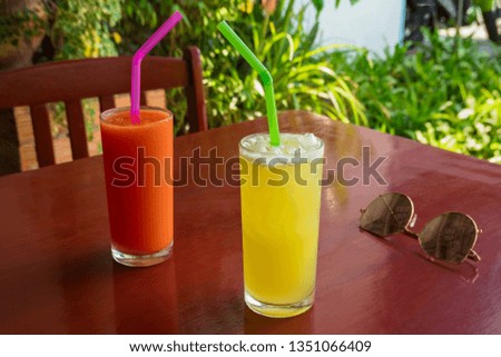 Juice Orange and tomato shake on the wooden table in restaurant with blurry tropical green leafs.