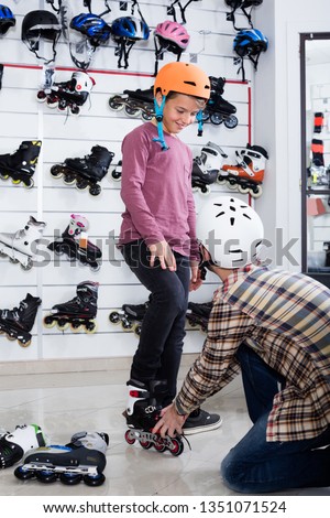 Man 29-39 years old helping his 9-14 years old son to try on roller-skates in sports store. 