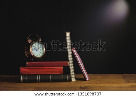 Still life old text book and alarm clock on table.