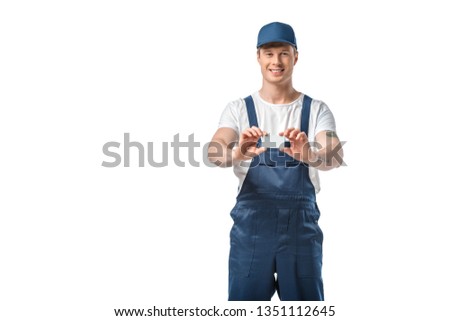 handsome mover in uniform looking at camera and holding blank business card isolated on white with copy space