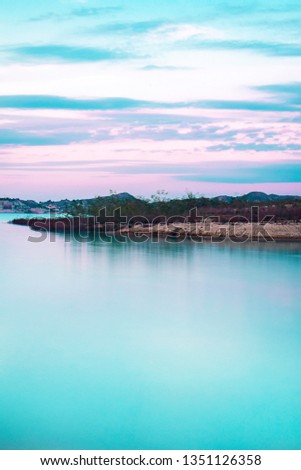 Long exposure picture from milky water of lake against at sunset. Dramatic sky with pink colors