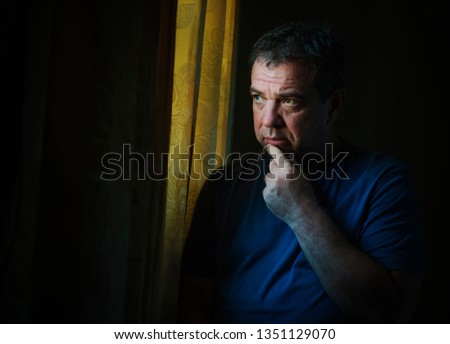 Sad mature man by the window in a dark room