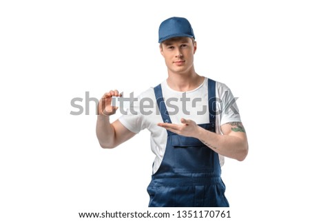 handsome mover in uniform holding blank business card and gesturing with hand isolated on white