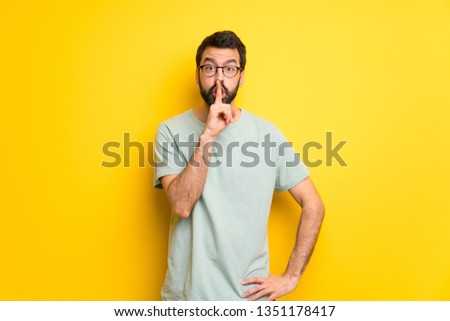 Man with beard and green shirt showing a sign of silence gesture putting finger in mouth