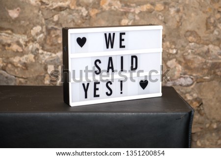 Lightbox /lightboard with text: We said yes! on black underground and stone wall in background.