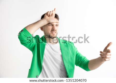 Losers go home. Portrait of angry guy showing loser sign over forehead in cause of victory and laughing over gray background