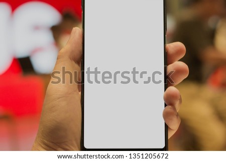 Mockup image of a man's hand holding black mobile phone with blank desktop screen on thigh in cafe, shopping online concept