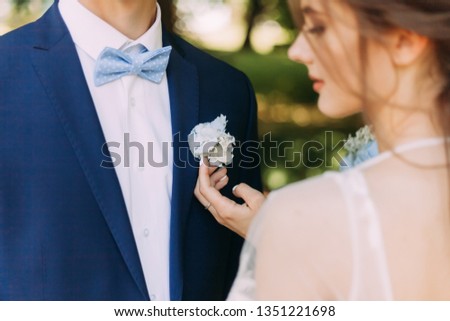 the bride gently touches the groom's boutonniere. wedding day. blue jacket with boutonniere