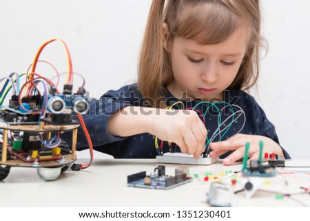 A cute girl constructs metal robot and program it. The boards and microcontrollers are on the table. STEM education inscription. Programming. Mathematics. The science. Technologie. DIY.  Royalty-Free Stock Photo #1351230401