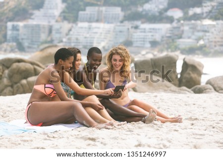 Side view of multi ethnic women reviving photos on beach while holding mobile phone