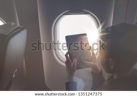 Caucasian boy fasten seat belt and using tablet pc and taking picture during air flight.  Safety travel with kid. concept 