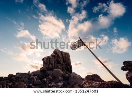jolly roger flag flies pinned between the rocks of the pirate island in front of a few clouds in the clear blue sky, Capo Testa, Santa Teresa di Gallura, Olbia Tempio, Sardinia, Italy