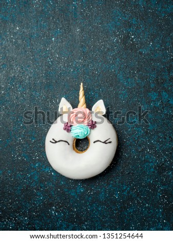 Unicorn donut over dark background. Trendy donut unicorn with white glaze. Top view or flat lay. Copy space for text. Vertical.