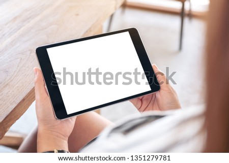Mockup image of a woman sitting and holding black tablet pc with blank white desktop screen horizontally