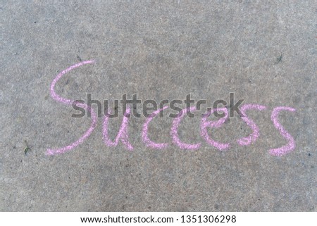 Success written with pink sidewalk chalk on gray concrete backgr