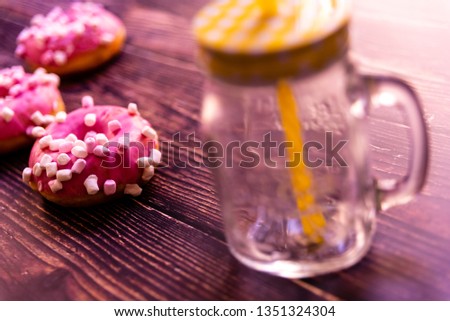 Pair of buns frosted with pink sugar and unhealthy marshsmallows next to a glass jar.