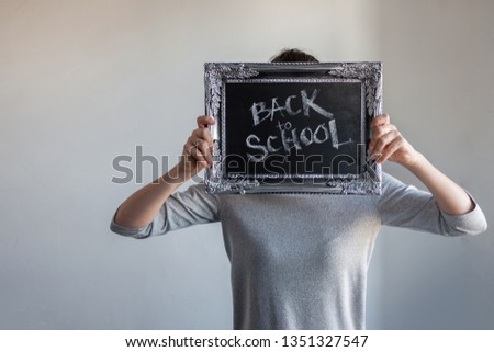 Back to school, Text on chalkboard in a vintage frame in the hand of a girl student. Student holds a sign at face level
