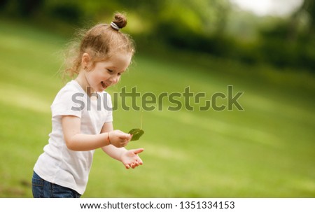 Copy space. Happy childhood. Emotional portrait of a positive and cheerful little girl playing with a smile with a leaf against the background of a lawn. Summertime. Summer vacation in nature