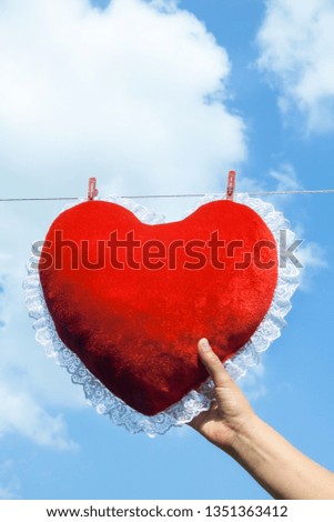 Red heart shaped cushion (pillow) hanged on the clothes line and fastened with a clothes pegs against the blue sky.