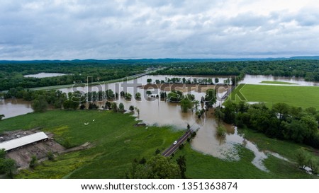 Aerial View of Rural Farm affected by Spring flooding featuring Farm house, silo on dry ground, livestock, green fields, brown flood water, covered roads