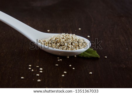 Close Up of Tan Quinoa Grain on white spoon with green leaf on dark wood background