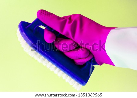 Hand in pink rubber latex glove holding a brush for cleaning surfaces, carpet, bathroom on yellow background, spring cleaning, space cleaning. the concept of bright spring and renewal, bright mood
