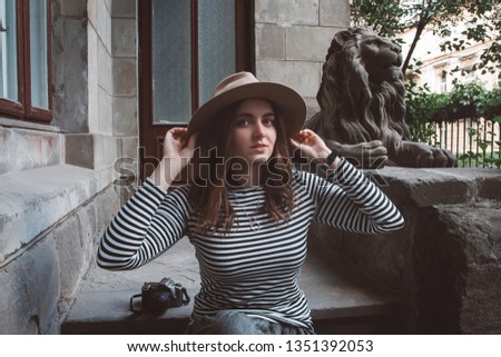 Beautiful woman in a striped shirt and hat. Holds the camera near the statue of a lion against the background of the old house