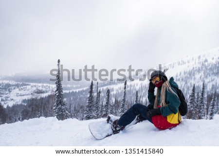 Woman snowboarder with a snowboard sit in the mountains on a snowy slope.