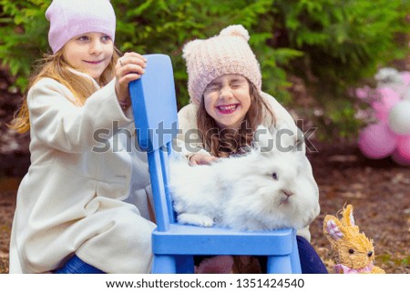 Cute, little girls, sisters, having fun in the backyard with white rabbit sitting on the blue chair.  Easter concept