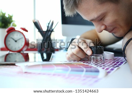 Male serviceman hold in hand magnifying glass making colour test at worktable for further promotion closeup