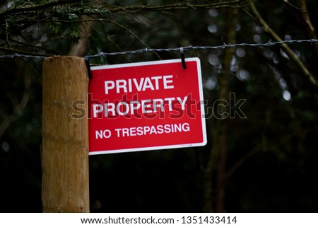 Private property no trespassing sign fixed to barbed wire fence protecting woodland with shallow depth of field