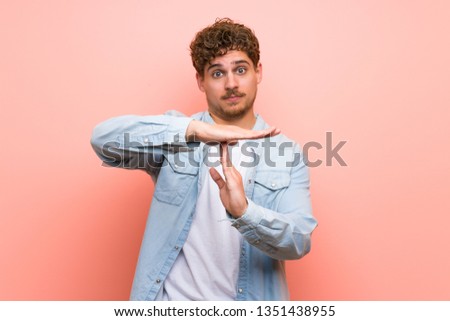 Blonde man over pink wall making stop gesture with her hand to stop an act