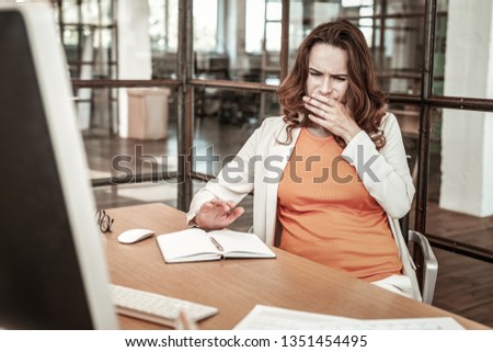 Office computer. Dark-hired pregnant woman being sick and having digestion problems while making notes on working place Royalty-Free Stock Photo #1351454495