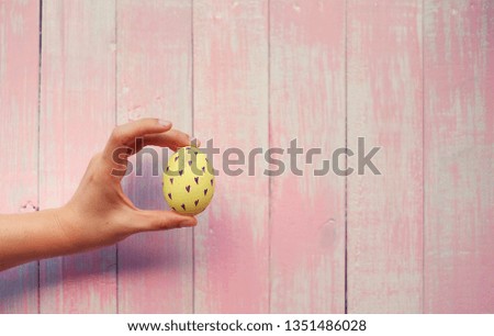 A hand holding a colorful hand painted easter egg with pink distress wooden background, pastel color egg with a unique pattern.