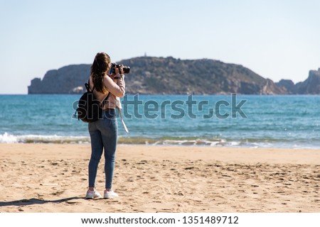 Back view of woman taking pictures with DSLR camera of islands from the beach - Medes Islands