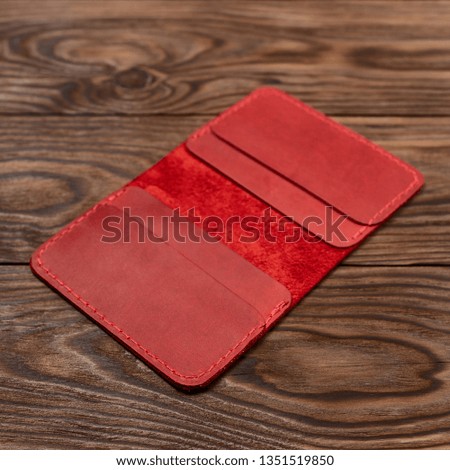 Handmade red leather cardholder on wooden background. Cardholder have 4 pockets for cards. Stock photo with soft focus background.