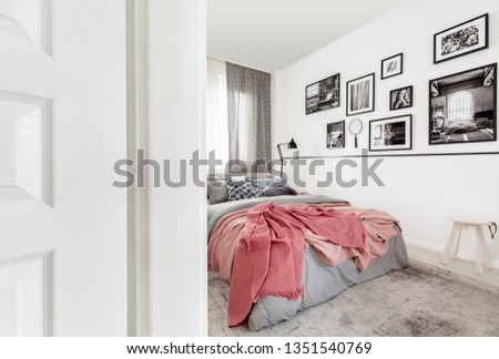 Gallery of posters on white wall in modern bedroom interior with pink sheets on bed. Real photo