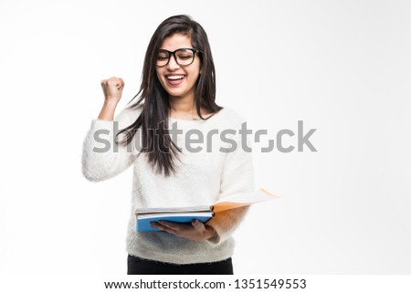Portrait of attractive indian student woman standing holding reading a book with win gesture over white background.