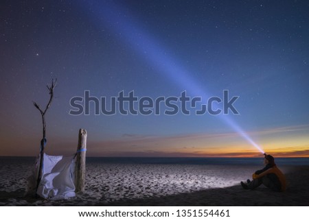 A young man sitting on the sandy beach, relaxing and enjoying the deep night and the starry sky.