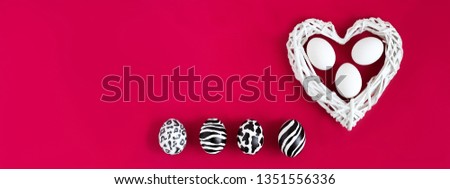 Set of three easter eggs painted like zebra, cow, snow leopard. Three white eggs inside a white heart wicker from twigs on red background. Top view. Banner.