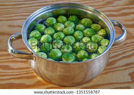 Close up picture of stainless steel cooking pot with water and bunch of fresh harvested green brussels sprouts before cooking on wooden table. Light and healthy vegetarian, vegan dish full of vitamins