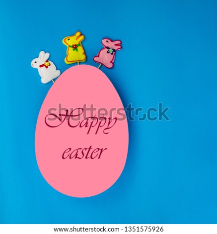 Easter eggs. Happy easter card. A large pink egg with an inscription Happy Easter. Three multi-colored bunny. on a blue wooden background. Copy space