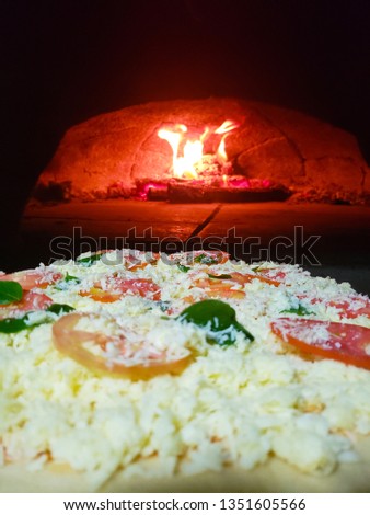 Pizza being placed to bake in the wood oven. In the background wood on fire