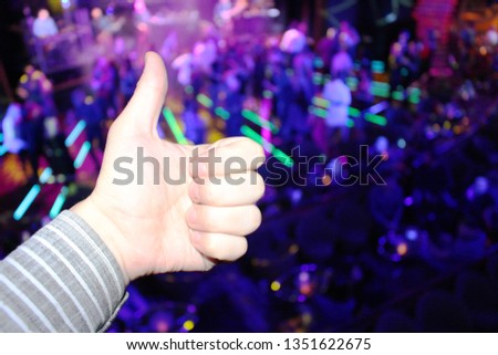 A hand showing a class sign on the background of a laser show at a disco on a cruise ship. The background is dominated by purple and blue lights.
