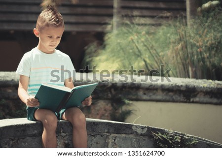 Young boy in t shirt reading book in a beautiful Church garden