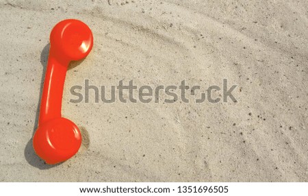 Red alarm tube of an old vintage phone is lying on the sand with a copy space for your text with contacts.